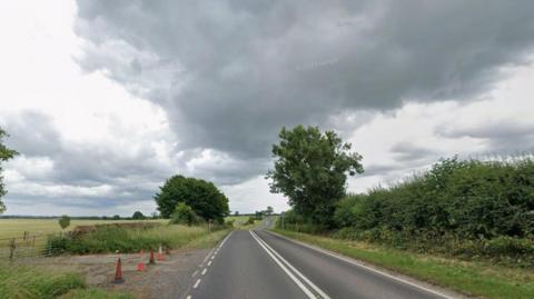 Road with fields on one side and a hedge on the other