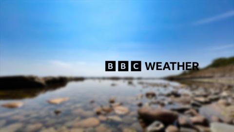 The BBC Weather logo overlaid on a photo from Crail in Fife. Blue skies overhead a still body of water with rounded pebbles.