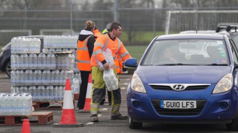South East Water workers in hi vis hand out bottled water to drivers at East Grinstead Rugby Club.