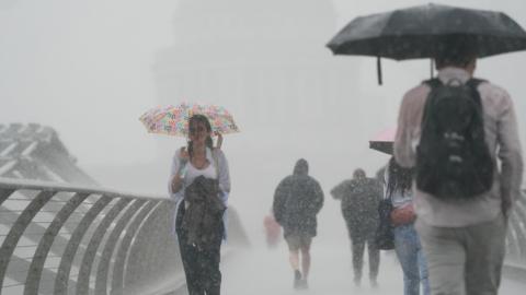 People walk across Millennium Bridge in London in torrential rain