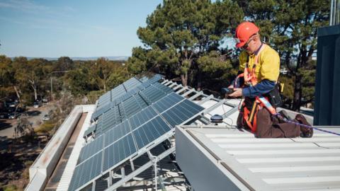 Stock image of a man installing solar panels on a roof