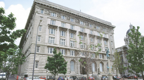 Liverpool City Council's headquarters, the Cunard Building. It is a five-storey, stone-built building surrounded by young trees. 