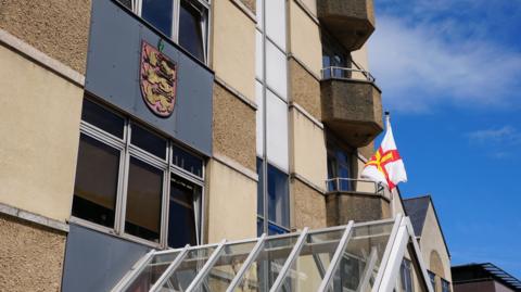 Frossard House - A building with the States of Guernsey logo and a Guernsey flag flying outside it. 