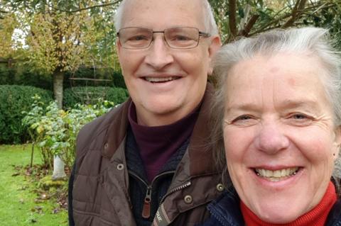 A selfie of Debs (taking the picture) and Simon. Debs has grey hair, tied back, and wears a blue coat and red polo neck. Simon has short white hair, and wears glasses and a brown coat.