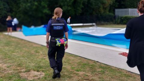 A woman TVP officer walking beside the Abbey Meadows outdoor pool. People can be seen around the pool in the distance, handling its covers.
