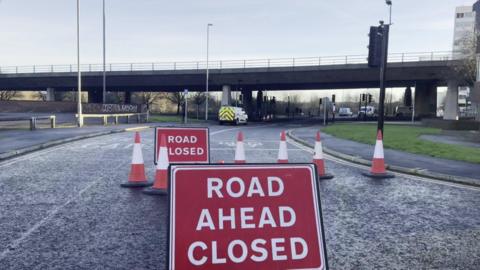 Two road closure signs placed in the middle of the road ahead of the Gateshead flyover. Traffic cones block the road. The concrete bridge can be seen in the background.