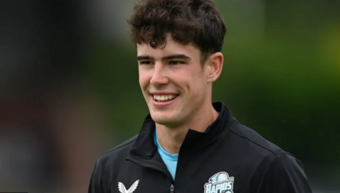 Late cricketer Josh Baker, a young man with dark curly hair, smiles while looking off-camera. He is wearing a black Worcestershire Rapids top.