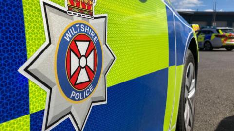 A close-up image of a yellow and blue Wiltshire Police car bearing the Wiltshire Police crest.