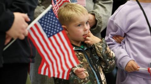 People from the first group of white South Africans granted refugee status in the US hold US flags as they attend a meet and greet event, at Dulles International Airport