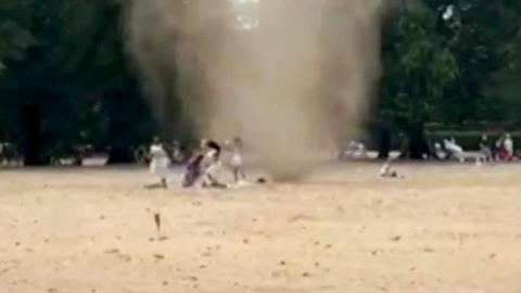 A dust-filled whirlwind is seen spinning through a brown and yellow park in London with people getting out of the way in a grab from video