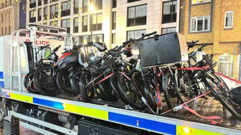 Rows of seized e-bikes on a police transportation vehicle.