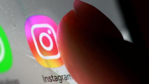 A thumb hovers over a smartphone displaying the purple, yellow and orange Instagram logo