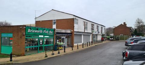 A white-fronted building with grey horizontal shutters. There is a red brick extension which houses a fish and chip shop. 