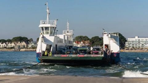 Chain ferry approaching slipway in choppy seas with buildings and shore in background