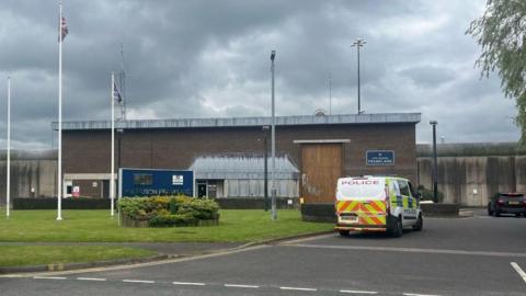 A police van parked outside HMP Frankland. The building consists of a large brown brick wall with a large brown door for vans.