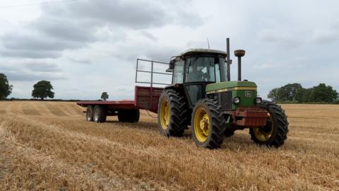 A farmer in a green tractor pulling a red trailer