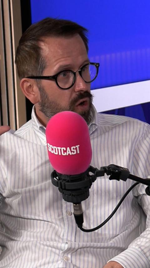 Man in white shirt with beard and glasses in front of red microphone
