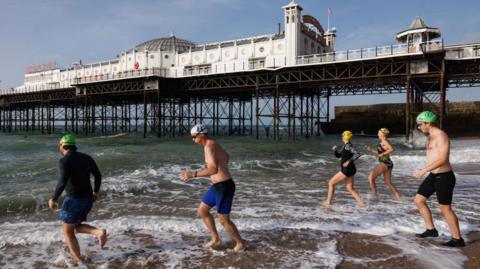 Swimmers running into the sea next to Brighton Pier