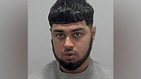 Police mugshot of Hamza Arshad. He has dark hair, a dark beard and is wearing a grey sweatshirt