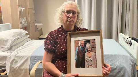 Julie Whittaker wearing a maroon pattern top, holding a framed picture of her parents