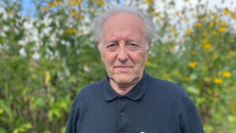 Older man with white hair wearing a dark polo top