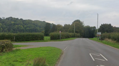 A road junction with no vehicles on it and grass and bushes on both sides