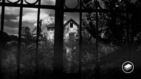 A haunted house behind a closed iron gate. 