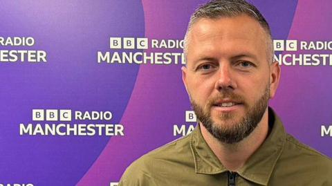 Robert Kenyon with short grey hair and beard wearing an olive coloured jacket