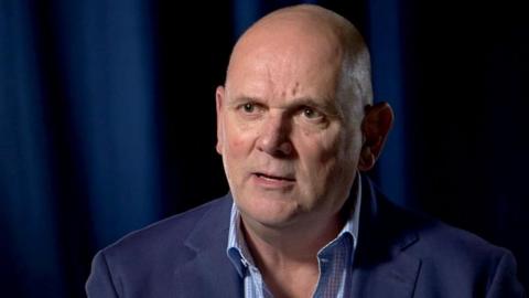 Jim Gamble, wearing a blue shirt and jacket, speaks to the BBC in 2022