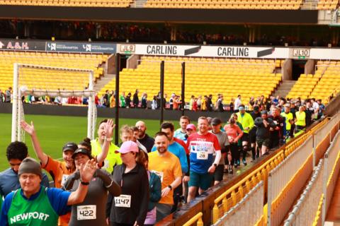 People dressed in running gear inside a football stadium that has bright yellow seating.