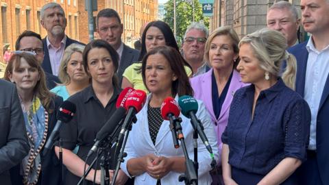 A media huddle of Sinn Féin politicians at a press conference