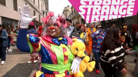 A clown in a parade and the Strange logo