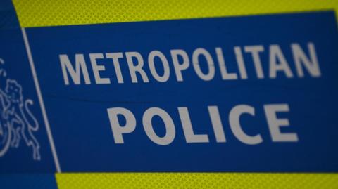 A close up of the livery on a Met police vehicle. It is blue with white letters and a yellow stripe. 