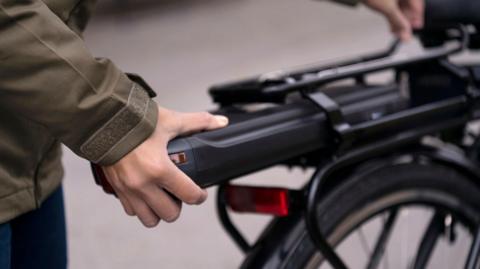 A person changing the battery on the back of an electric bike