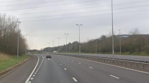 Cars are driving along a motorway with trees lining each side of the road 