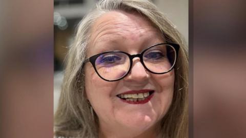 Debra Tracey, a woman with large round reading glasses and and a bright smile. She has long blonde hair.