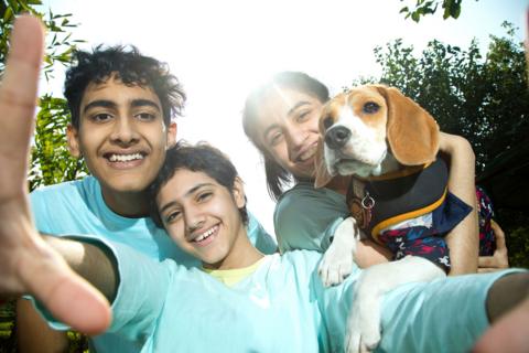 three children take a smiiling selfie with a beagle dog in the sunshine
