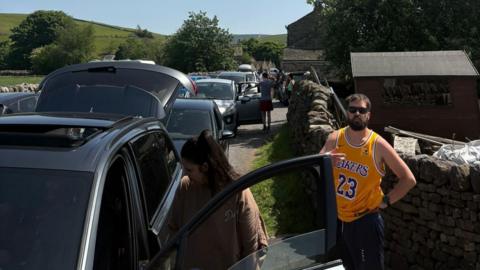 A large number of cars parked on a small lane in a village in the Yorkshire Dales