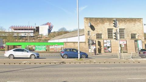 A stone two-storey warehouse frontage sits alongside a busy road.