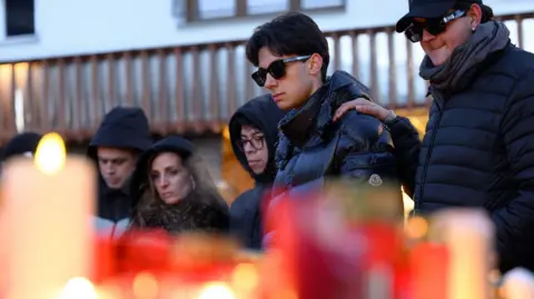 People stand by candles and flowers, laid for victims of a fire
