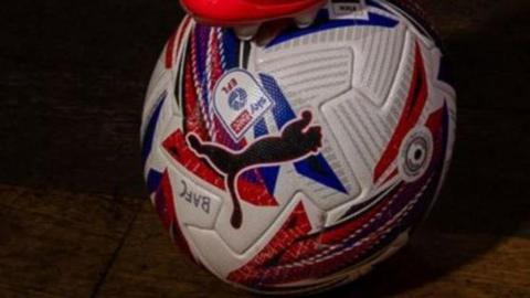 Close up of a white football with black blue and red shapes, and written in ink "BAFC".