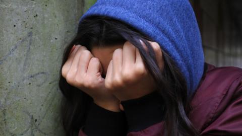 A young person wearing a blue hoody burying their head in their hands in a state of emotional distress. 