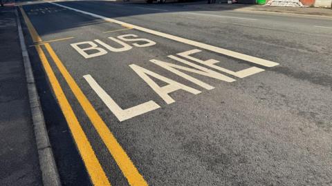 White Bus Lane painted onto tarmac road, by two double yellow lines