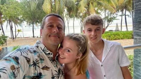 An image of Izzy, her dad and brother on a beach abroad