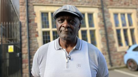 Lloyd Russell is standing in front of the former site of Empire Fighting Chance's gym, where he trained since the 60s. He is wearing a cap and a grey t-shirt.