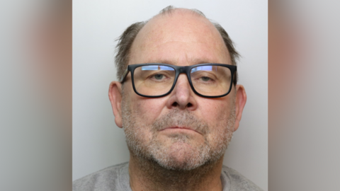 A mugshot of Martin Chubb, who is wearing a grey T-shirt. He is unshaven and balding. He has dark glasses.