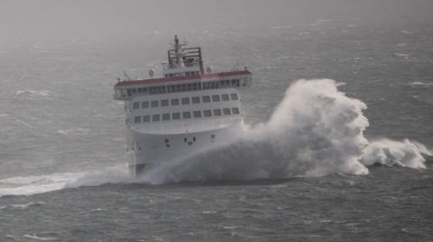 The Manxman ferry in rough seas with a large wave breaking at the front.