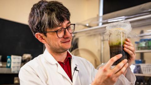 Man looking at scientific beaker with green substance