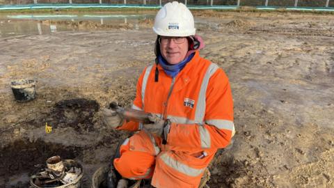 A man with glasses, an orange jumpsuit, and a white hardhat on.