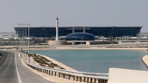 An exterior view of Doha's Hamad airport showing a lake in front of a terminal